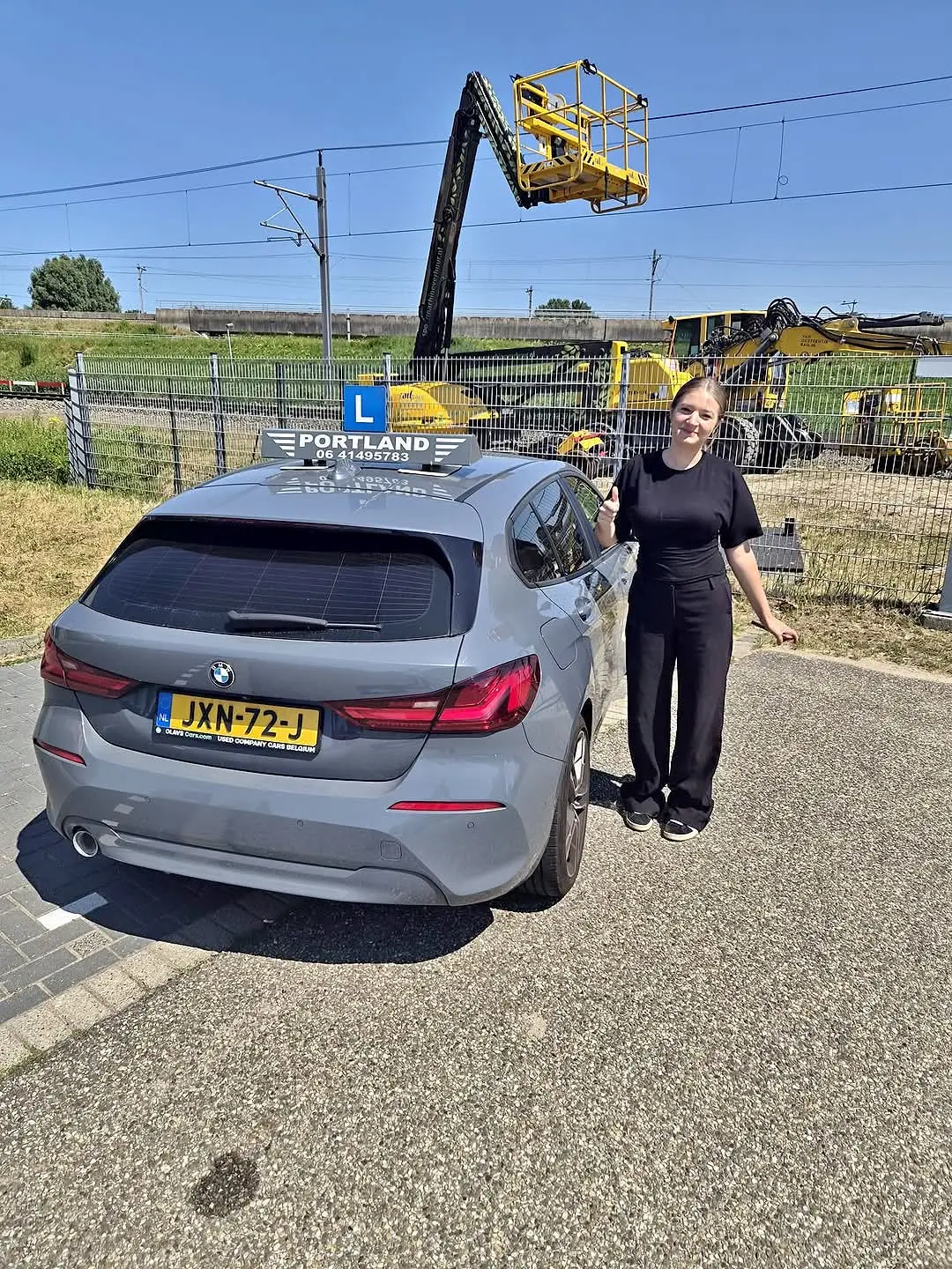 Een leerling poseert naast een lesauto van de rijschool met een duim omhoog