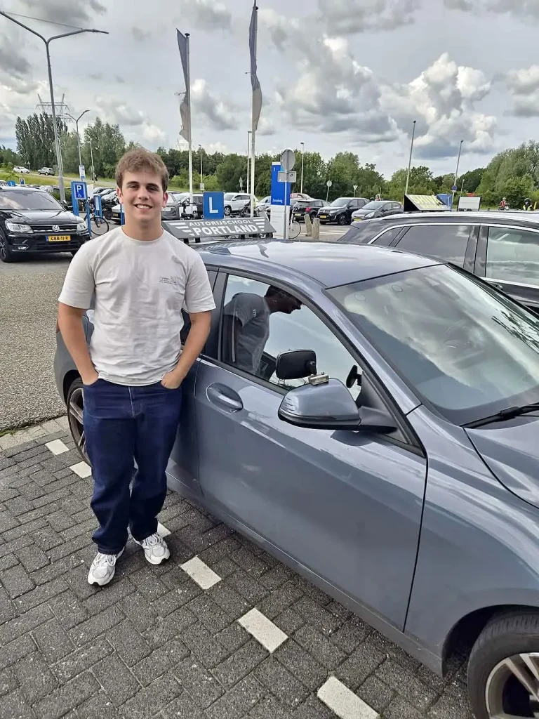 2a2c7b6c-f772-49c2-bf01-8c926754848d Een trotse leerling staat naast een lesauto van autorijschool Portland na het behalen van zijn rijbewijs