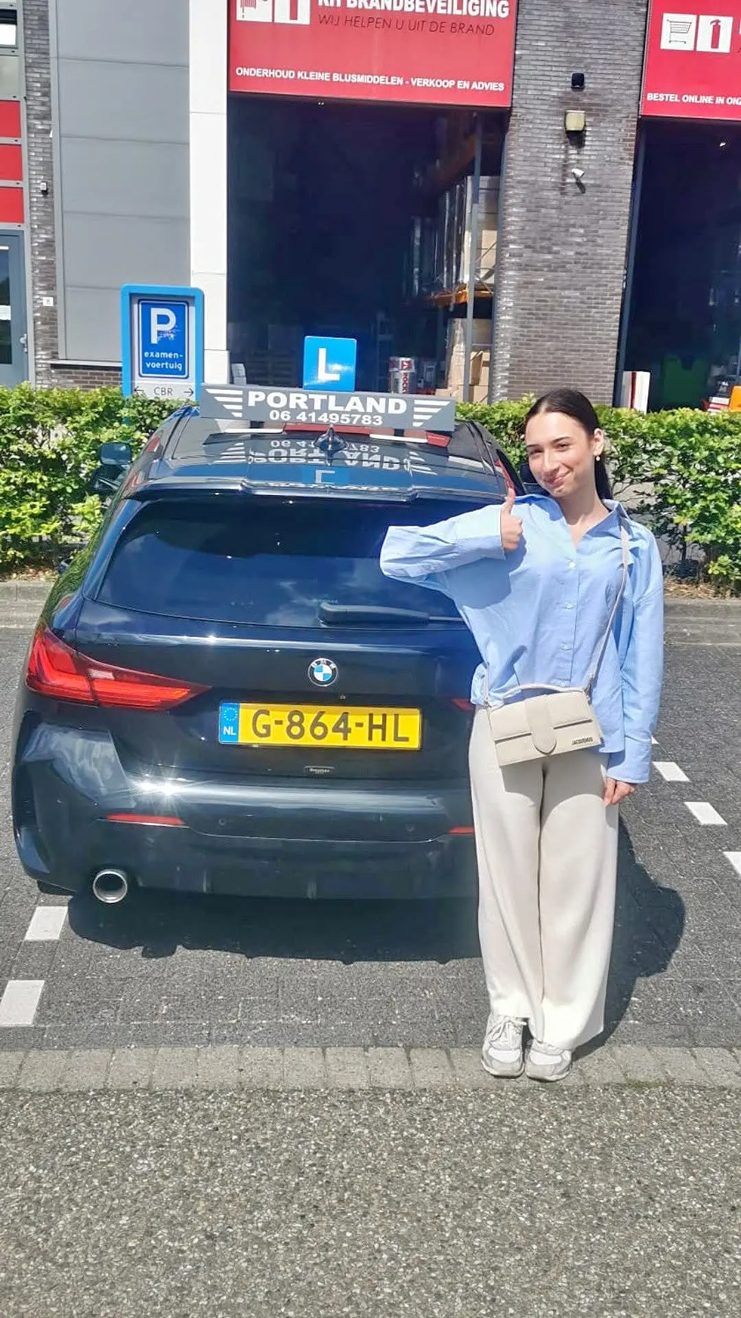 Een geslaagde leerling geeft een duim omhoog bij de lesauto