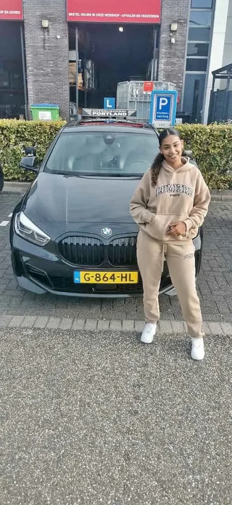 46f34596-5b09-42ae-ba89-130019797644 Een leerling staat blij naast een lesauto na het behalen van haar rijbewijs