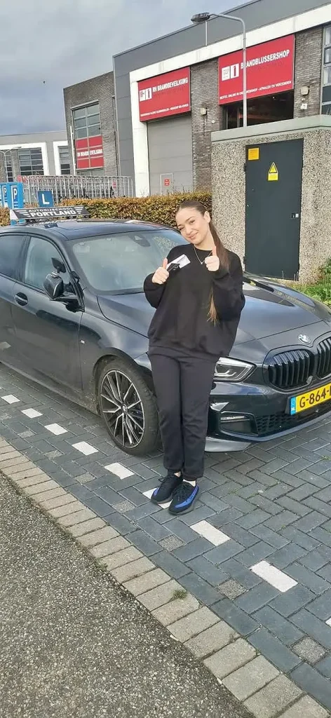 4a683afa-013b-476f-abd6-35a45f5f4684 Geslaagde leerling toont haar rijbewijs bij de lesauto