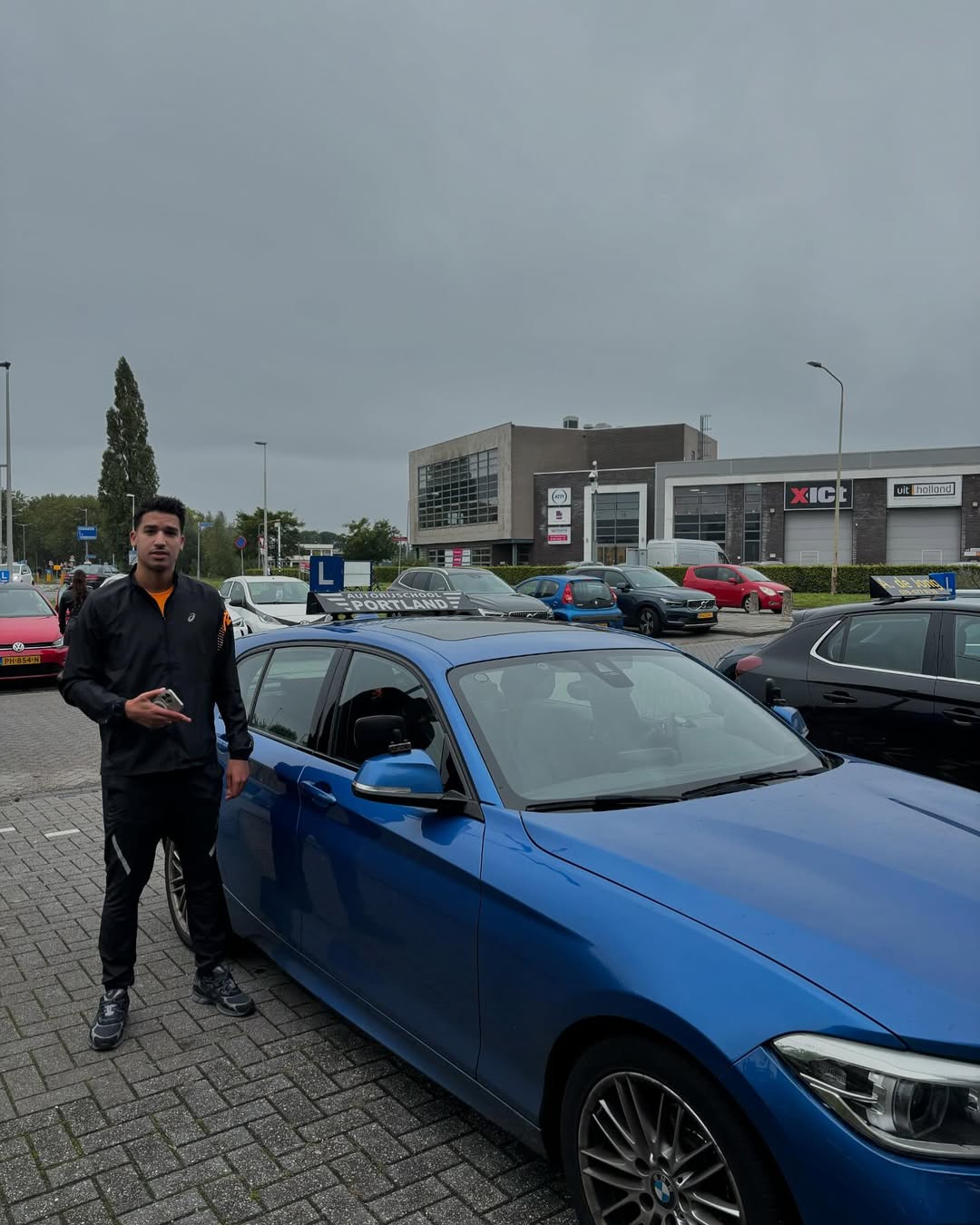 Een geslaagde leerling staat naast een blauwe lesauto