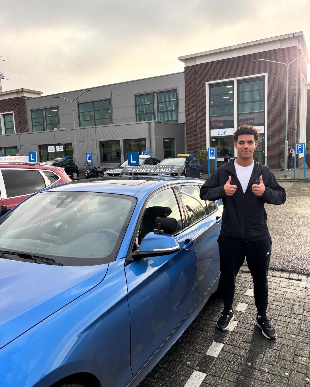 Geslaagde leerling geeft een duim omhoog bij de lesauto van Rijschool Portland