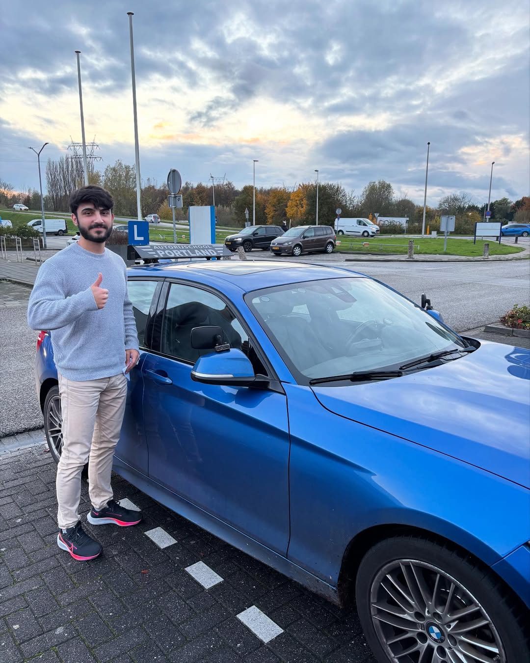 Een leerling geeft een duim omhoog naast een blauwe lesauto