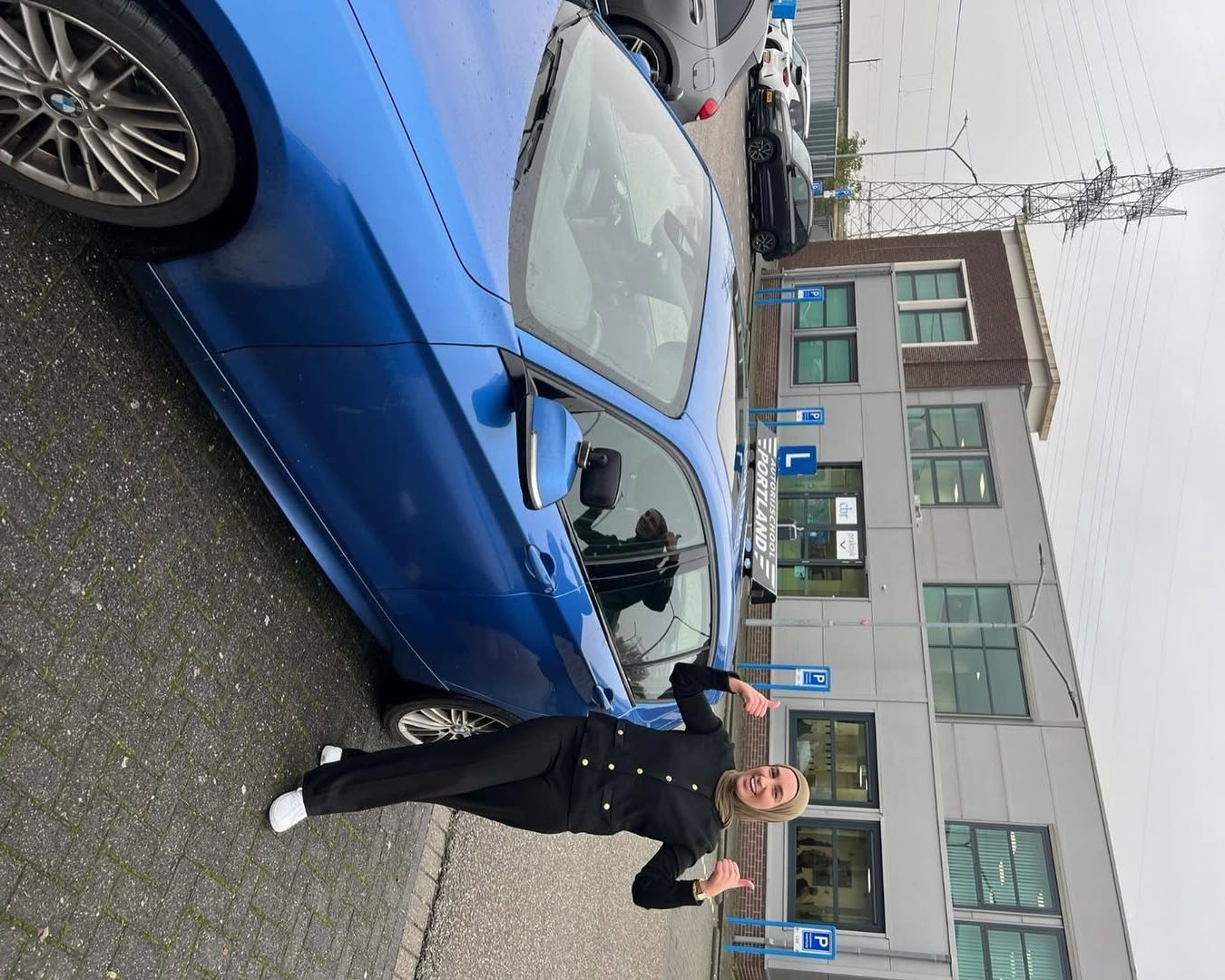 Een vrouw geeft twee duimen omhoog naast een blauwe lesauto