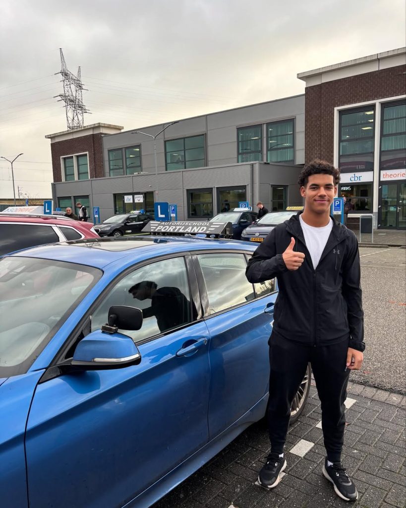 Geslaagde leerling geeft een duim omhoog bij een lesauto